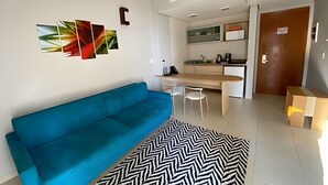 Ein modernes Wohnzimmer mit einem blauen Sofa, einem schwarz-weißen Teppich und einer Küchenzeile mit Esstisch und Stühlen.