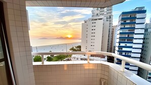 Ein Balkon mit Blick auf einen Sonnenuntergang über dem Meer, angrenzende Gebäude und ein Fliesenboden.