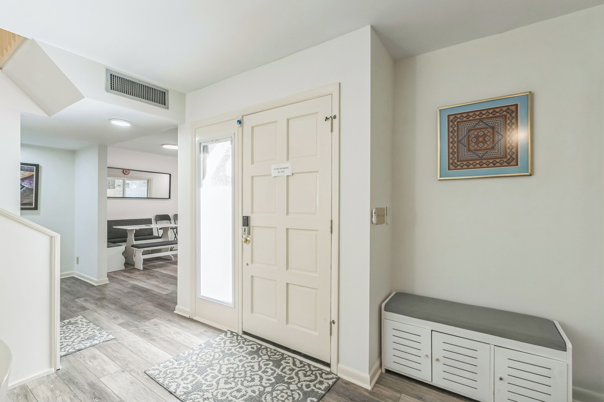 A hallway with a white door, a bench, and a patterned rug.