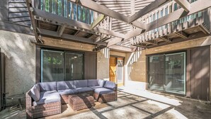 A modern outdoor patio with a sectional sofa, large windows, and a pergola structure.