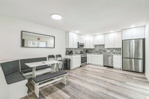 A modern kitchen with white cabinets, stainless steel appliances, a bench seating area, and a large mirror. - Mandarin Retreat: Pool-Hot tub-King Bed-Smart Tvs (Jacksonville)