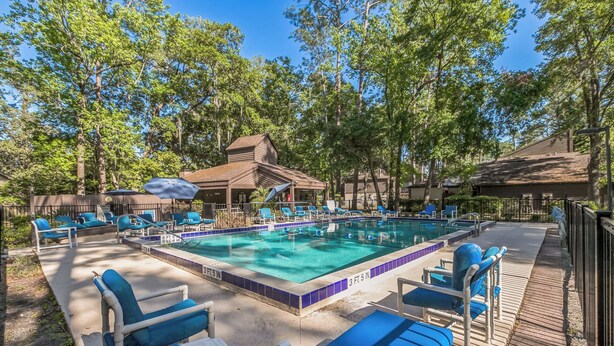 A swimming pool with lounge chairs, a wooden building, and trees in the background.