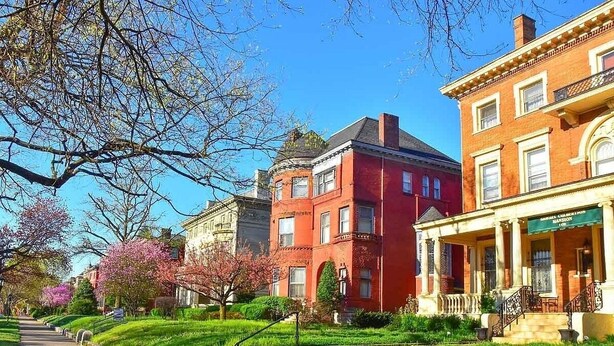 A row of historic buildings with a central red building, a green awning, and a well-maintained garden with a pathway. - Entire & Private Carriage House Near Downtown + 2 Complementary Housekeeping. (Louisville)