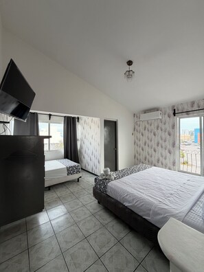 Een hotelkamer met twee bedden, een flatscreen televisie, een plafondventilator en uitzicht op de stad.