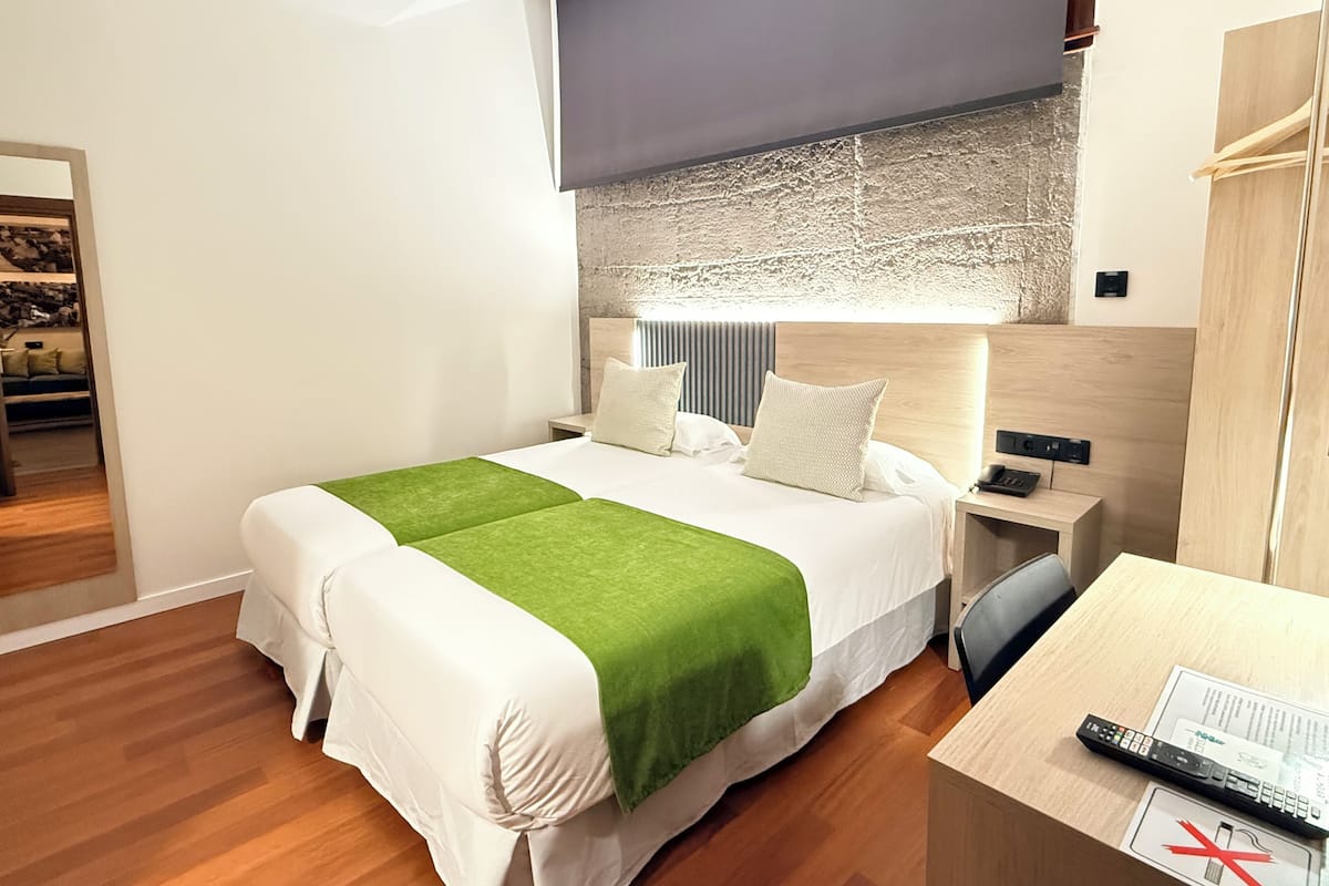 Habitación de hotel con cama, mesitas de noche, escritorio y vistas al exterior.