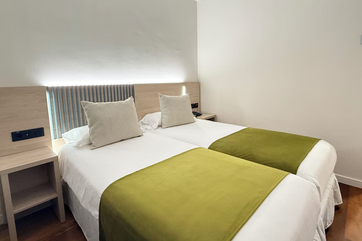 Una cama doble con dos almohadas, una mesita de noche y una manta verde.