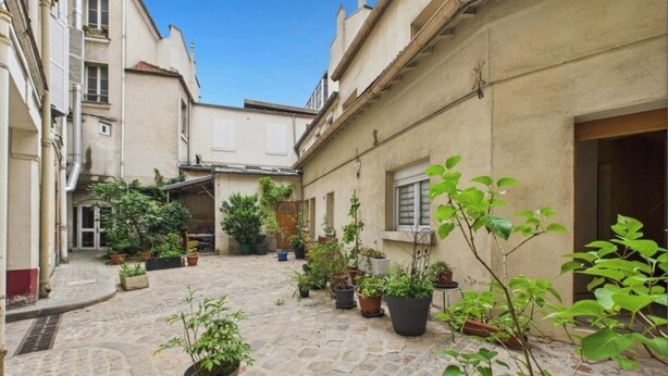 Un cortile con piante in vaso, pavimento in pietra e edifici con finestre e porte.