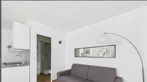 Un appartamento moderno con angolo cottura, un divano grigio, una lampada da terra e uno specchio a parete.