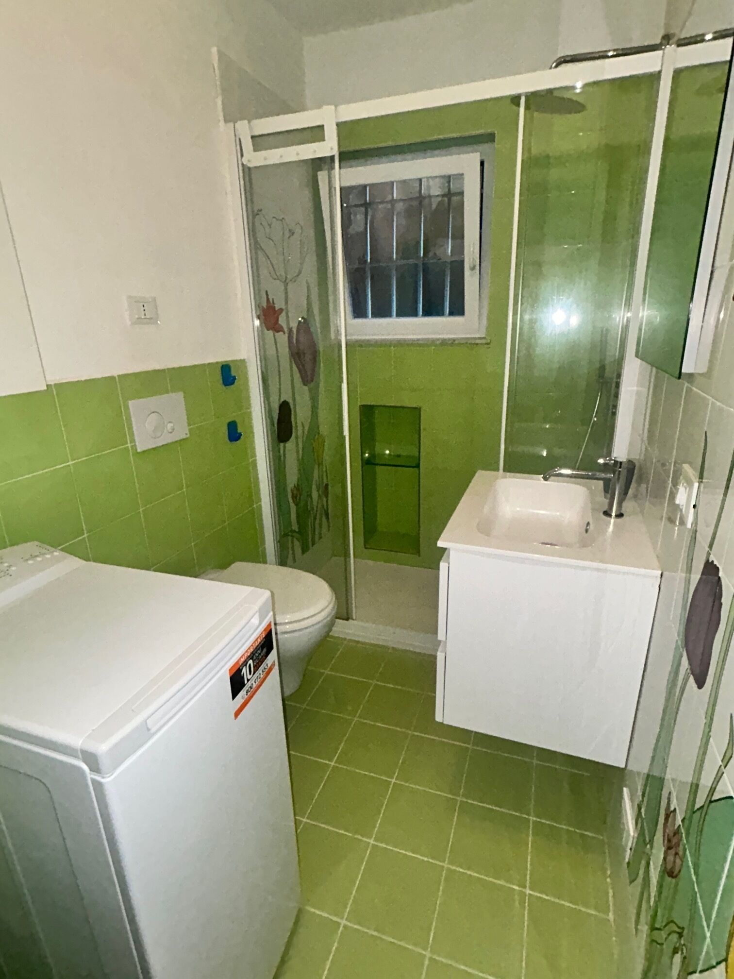Et badeværelse med toilet, brusebad, vask og vaskemaskine.