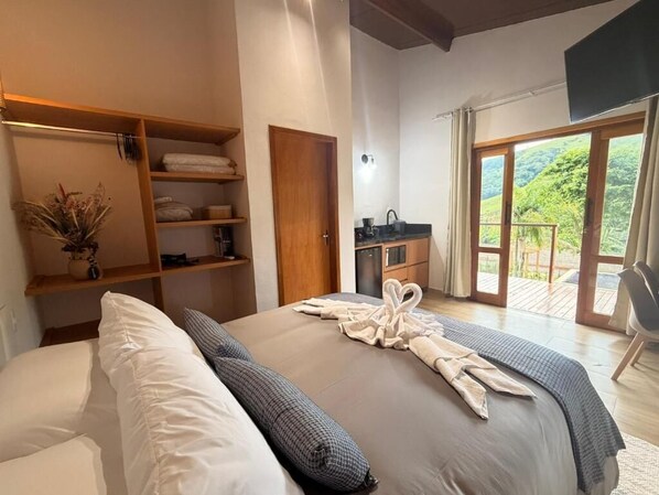 A bedroom with a bed, a wardrobe, a bathroom, and a balcony with a view. - Estúdios Entre Serras (São Bento do Sapucaí)