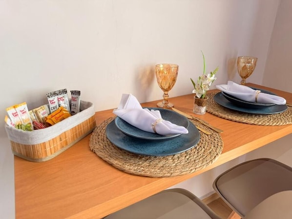 A dining table with two plates, a napkin, a basket of snacks, and two glass cups. - Estúdios Entre Serras (São Bento do Sapucaí)