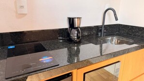 Una cocina con encimera negra, cafetera, lavabo y lavavajillas.