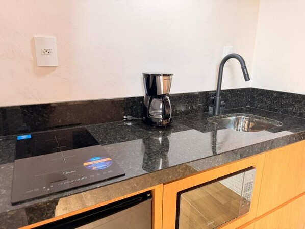 Una cocina con encimera negra, cafetera, lavabo y lavavajillas.