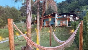 Una hamaca entre árboles en un área con césped, con una casa al fondo.