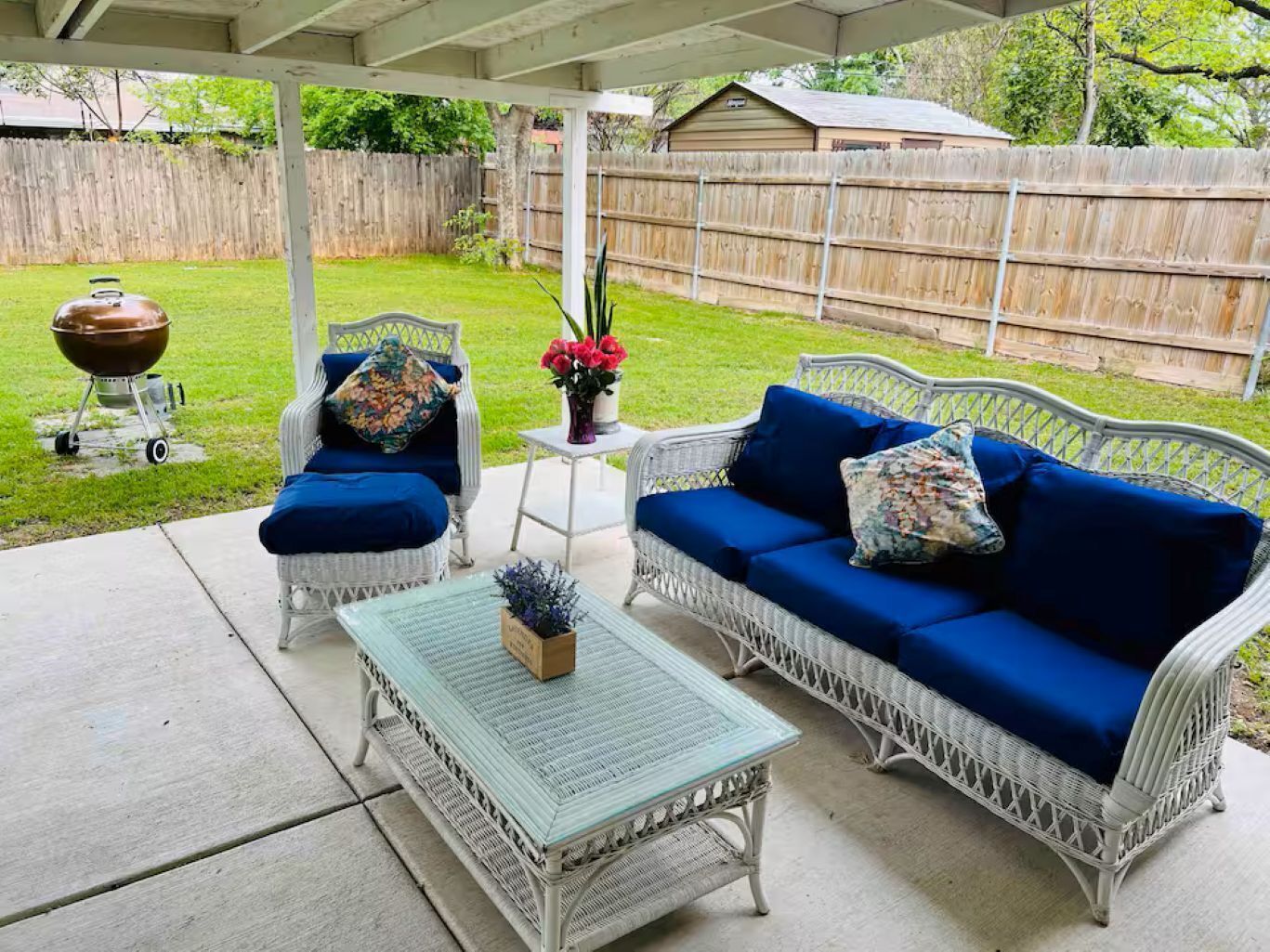A covered patio with wicker furniture, a small table, and a barbecue grill.