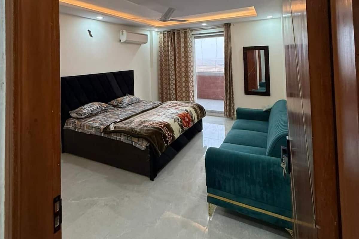 Un dormitorio con cama, sofá, ventilador de techo y ventana con cortinas.