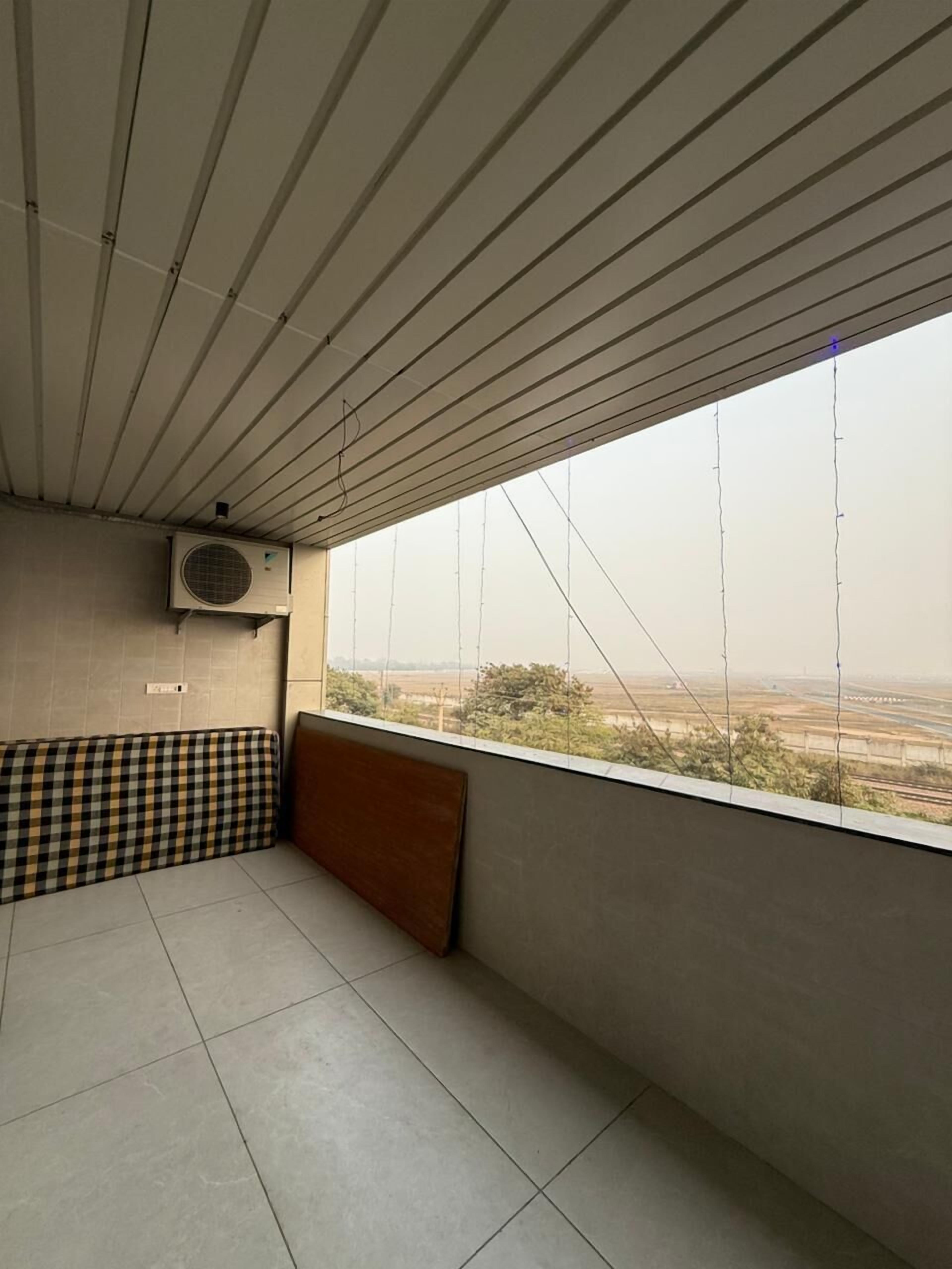 A room with a high ceiling, a large window, a checkered bench, and an air conditioning unit.