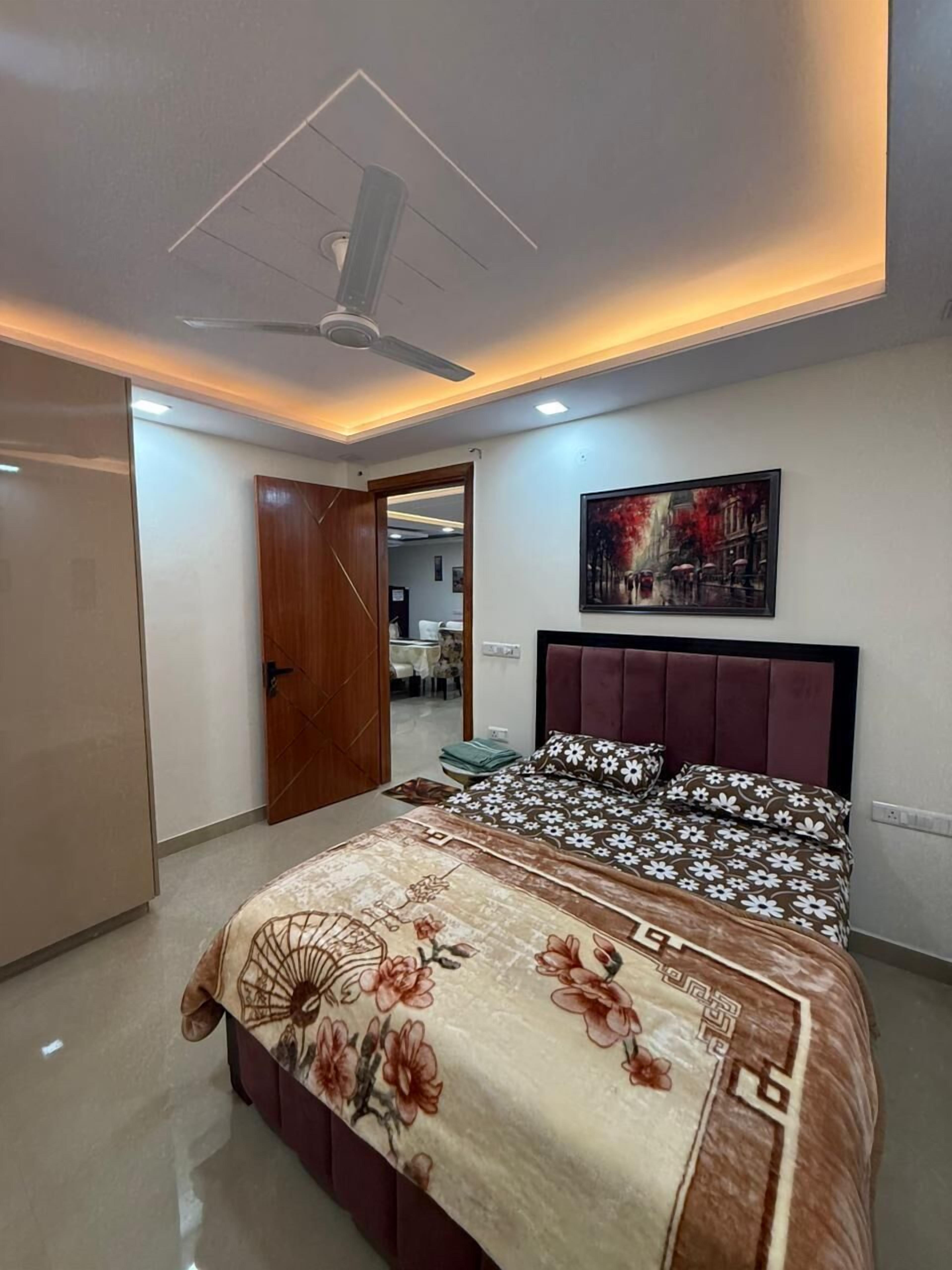 A bedroom with a bed, a ceiling fan, a painting, and a door leading to another room.