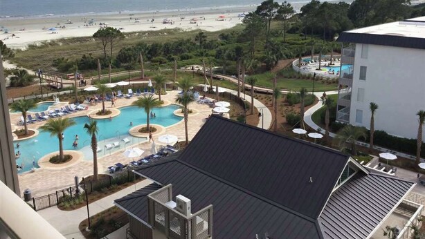 Ein Hotel mit Poolbereich, Blick auf den Strand und einem Gebäude mit geneigtem Dach.