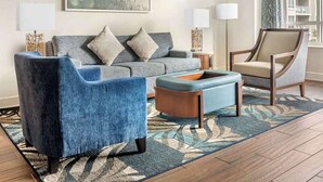 Ein Wohnzimmer mit Sofa, Sesseln, Hocker, zwei Beistelltischen und einer Stehlampe.