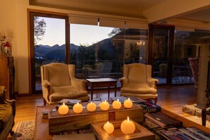 Amplia sala de estar con dos sillones, una mesita de centro con velas y vistas a las montañas a través de puertas de vidrio grandes.