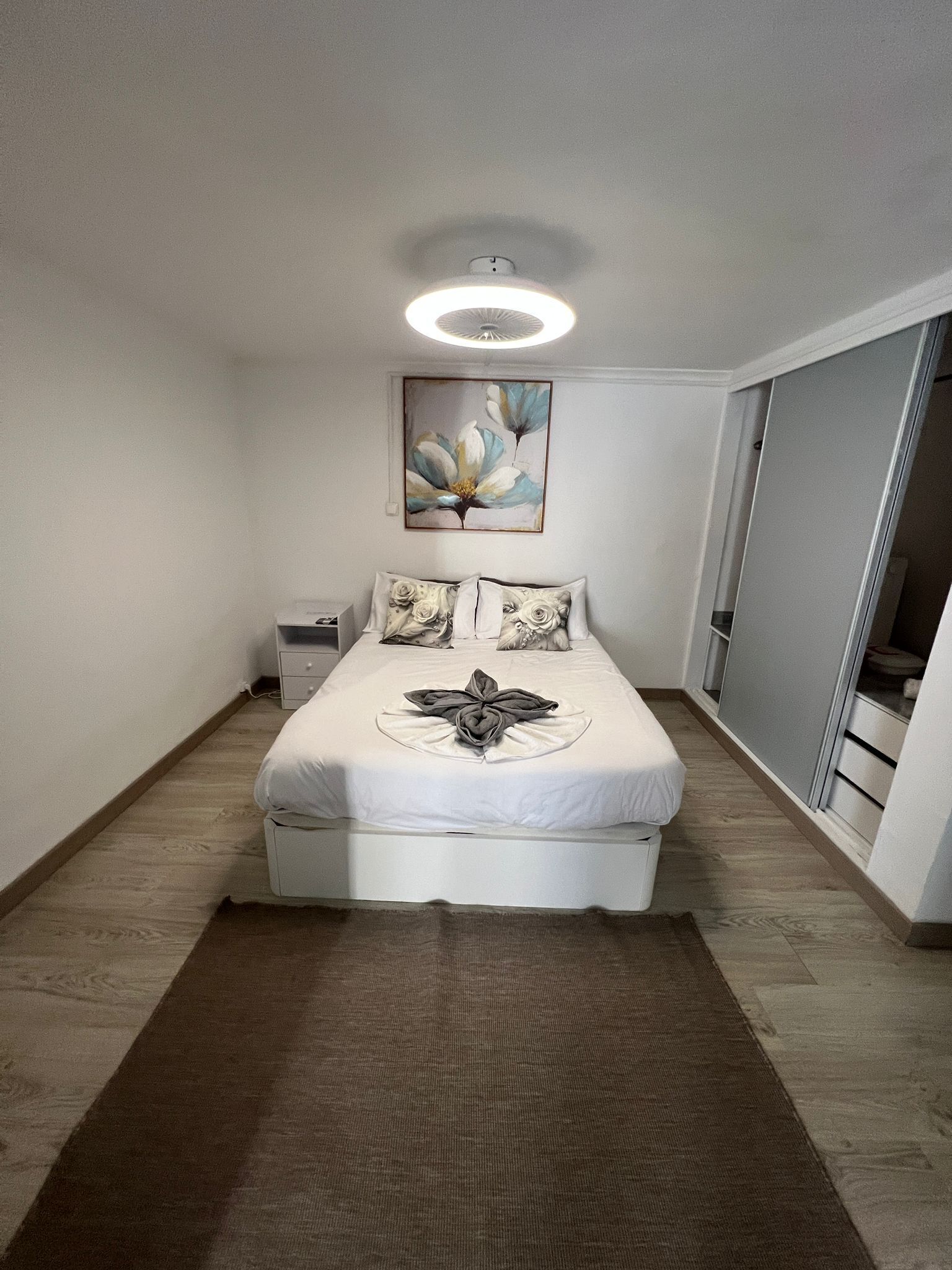 A bedroom with a bed, a nightstand, a painting, and a wardrobe.