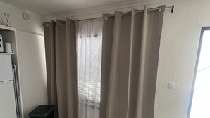 Una habitación con una mesa de comedor, un bote de basura, una ventana con cortinas y una puerta.