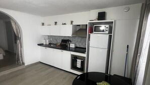 Cocina compacta con alacenas blancas, microondas, horno pequeño y una mesa de comedor con dos sillas.