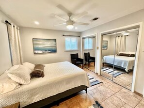 A bedroom with a bed, a ceiling fan, a painting, a chair, and a bathroom with a mirror and a bed. - Family Fun! Hot tub, Pool, Billiards, Gazeb (Richland Hills)