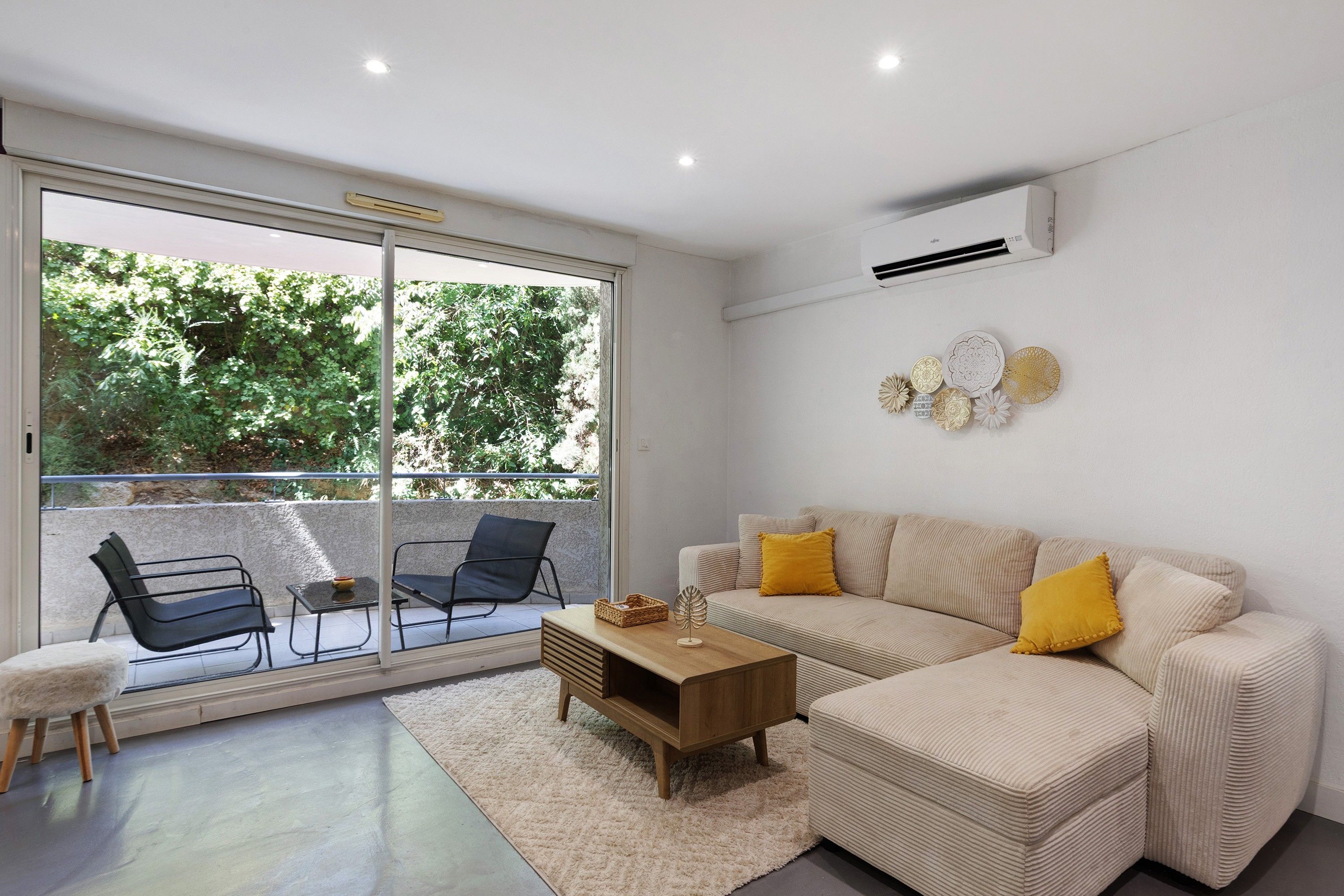 Uma sala de estar moderna com sofá, poltronas, mesa de centro e vista para uma área externa através de uma porta de vidro.