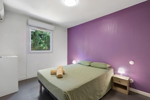 Una camera da letto con un letto, una finestra, un comodino e una parete in tinta unita.