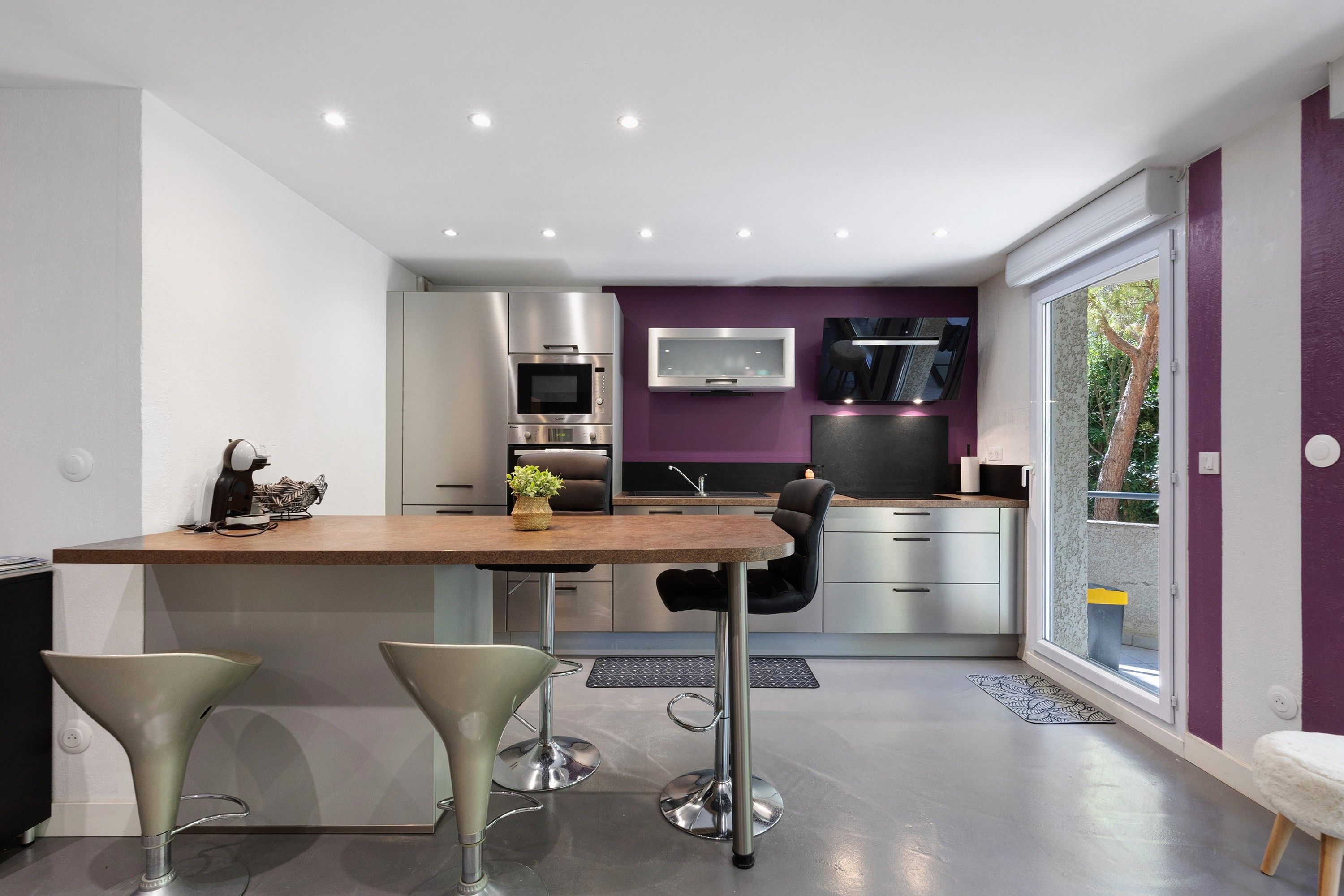 Une cuisine moderne dotée d’un îlot central, d’appareils électroménagers en acier inoxydable et d’un mur d’accent violet.