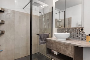Un bagno moderno con cabina doccia in vetro, uno specchio grande e un piano di lavoro in marmo.