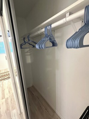 Un couloir avec un plancher en bois, un mur blanc et un portant à vêtements muni de plusieurs cintres.