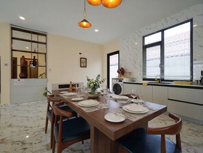 Ein Essbereich mit einem Holztisch, gedeckt für vier Personen, einer Küche im Hintergrund und einem großen Fenster mit Jalousien.