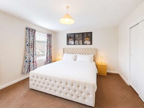 Un dormitorio con una cama grande, dos mesitas de noche, un ventanal con cortinas florales y una pared con cuadros enmarcados.