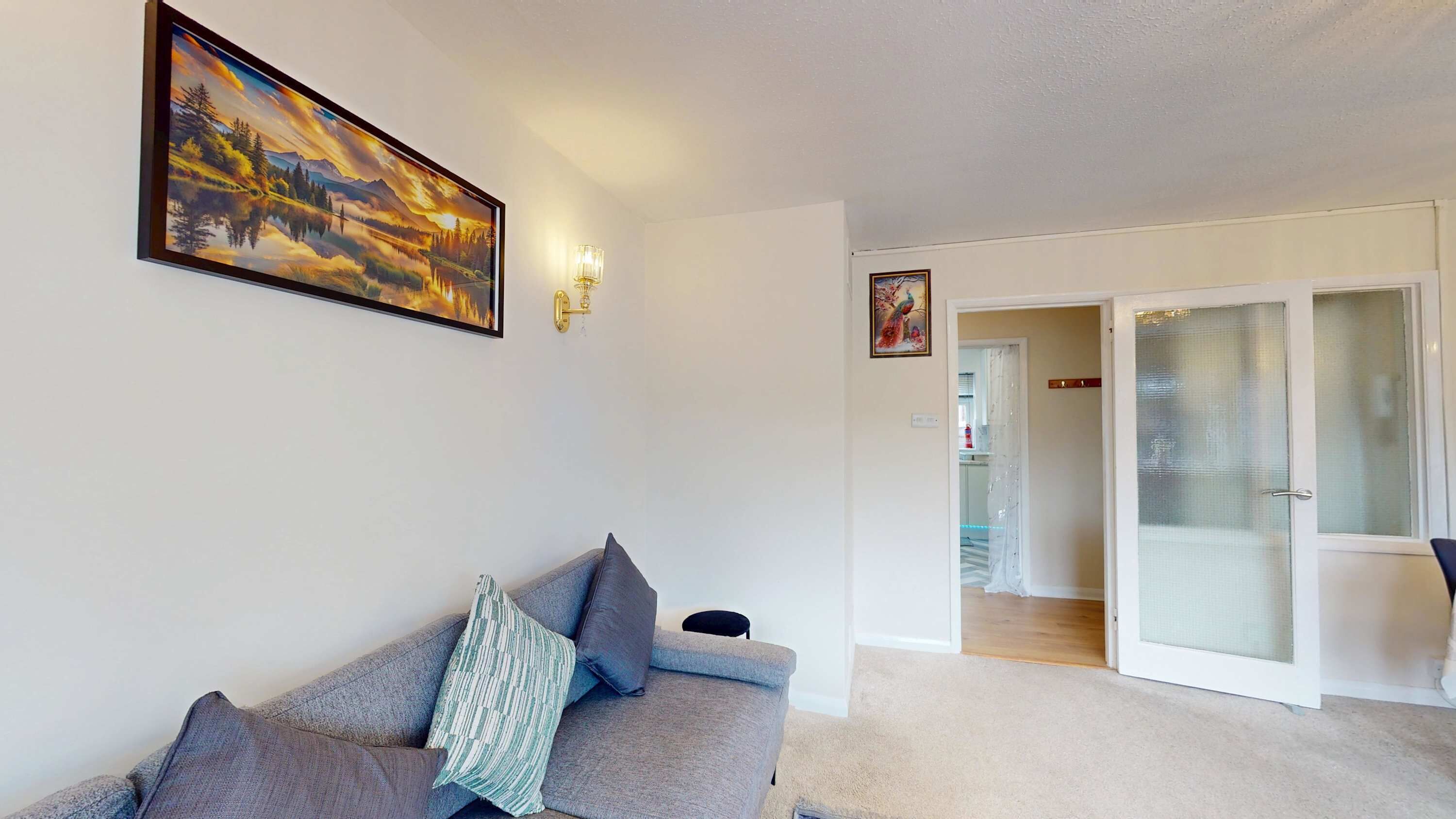 A living room with a sofa, a painting, and a door leading to another room.