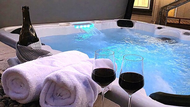 A hot tub with two glasses of red wine and a bottle of wine, surrounded by towels.