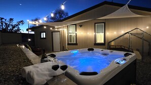 A hot tub with a blue light, a covered patio, and string lights.