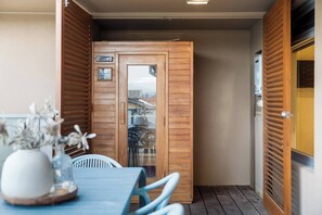 A small room with a wooden door, a table with chairs, and a vase with flowers. - Open Horizon Postcard Ocean Views and Sauna (Glenelg South)