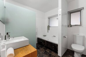 A modern bathroom with a white bathtub, a separate shower area, a toilet, and a wooden vanity with a towel. - Open Horizon Postcard Ocean Views and Sauna (Glenelg South)