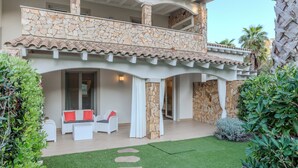 Une maison à deux étages avec une façade en pierre, un balcon et une terrasse aménagée avec du mobilier d’extérieur.