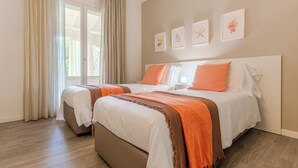 Un lit double avec une literie orange et blanche, une table de chevet et une fenêtre avec des rideaux.