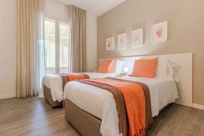 Ein Doppelbett mit orange-weißer Bettwäsche, ein Nachttisch und ein Fenster mit Vorhängen.