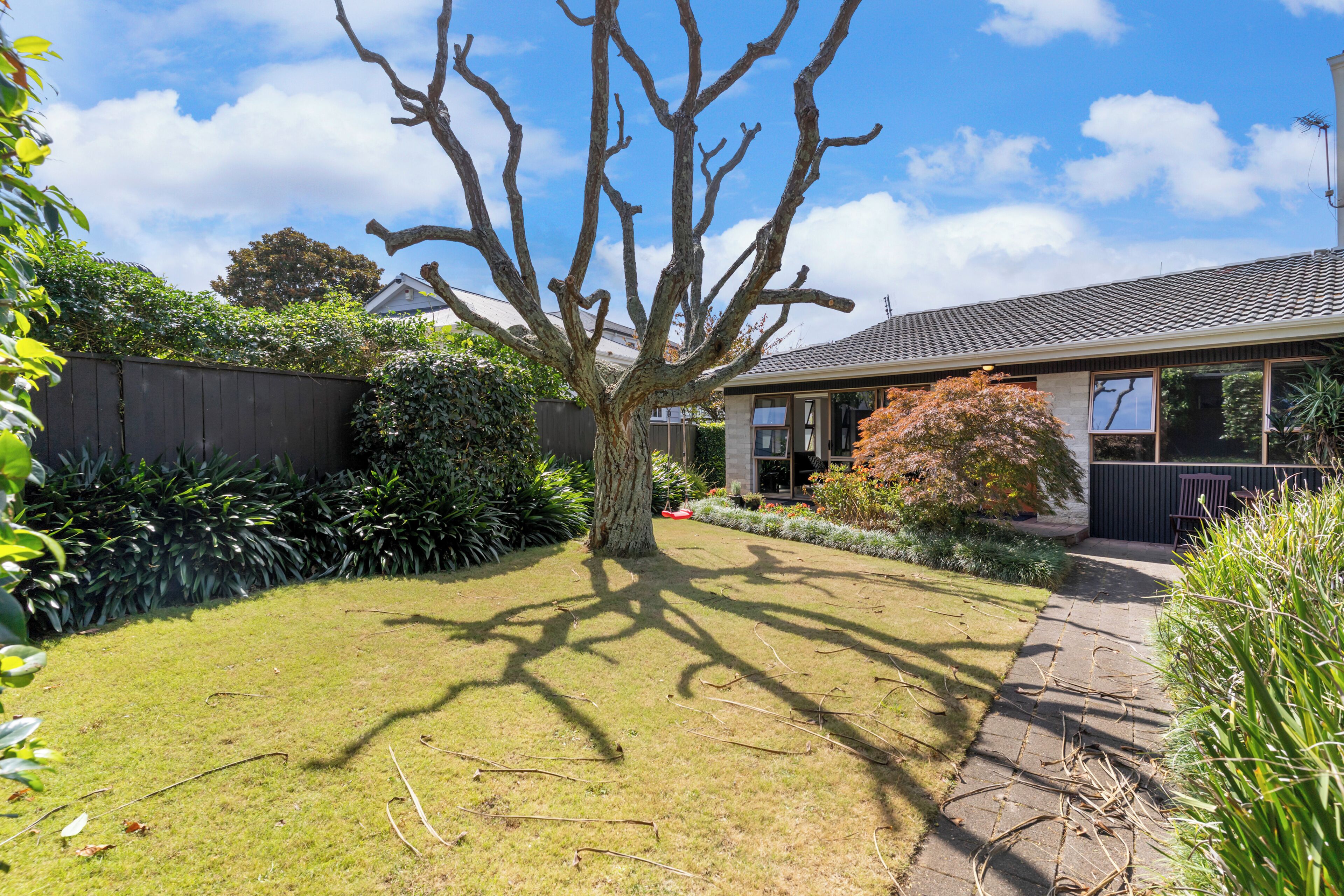 A residential property with a well-maintained lawn, a large tree, and a pathway leading to the house.