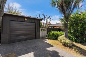 A garage with a closed door, a driveway, and a garden with various plants and a palm tree.