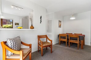 Een kamer met een eettafel, stoelen, een houten stoel met kussen, een spiegel en een vaas op een plank.