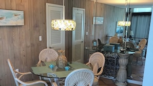 Un coin repas avec des chaises en osier, une table en verre et des luminaires suspendus.
