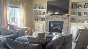A living room with a fireplace, a flat-screen TV mounted above it, and a sofa with multiple cushions. - Gorgeous 4-bedroom house with AC in charming Winneconne (Winneconne)