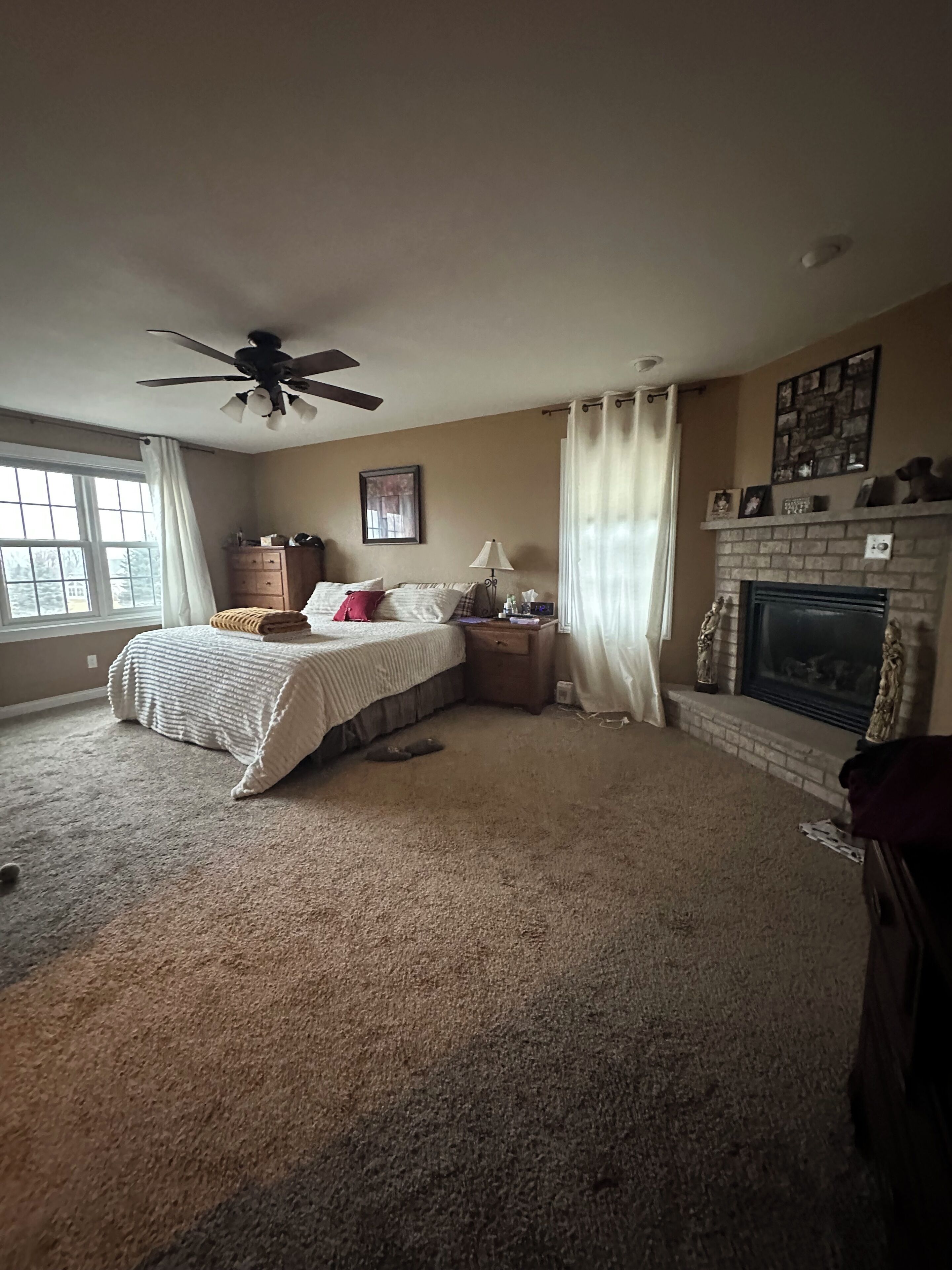 A bedroom with a bed, a ceiling fan, a fireplace, and a window.